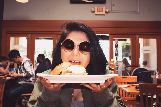 Woman at restaurant holds up a plate with cheeseburger to her face