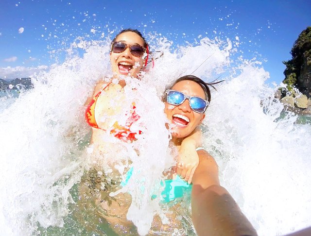 Two happy young people take a selfie as they're hit by a wave on the beach
