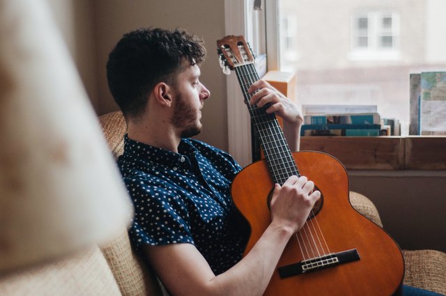 Young white man playing acoustic guitar on couch