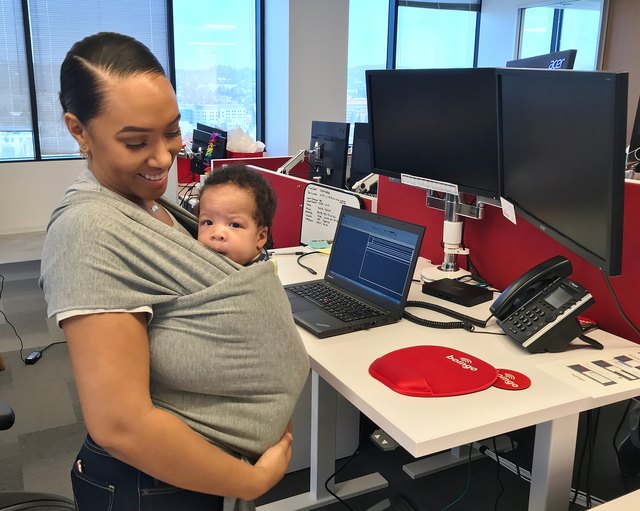 Young Black mother wearing an infant in a sling in an office