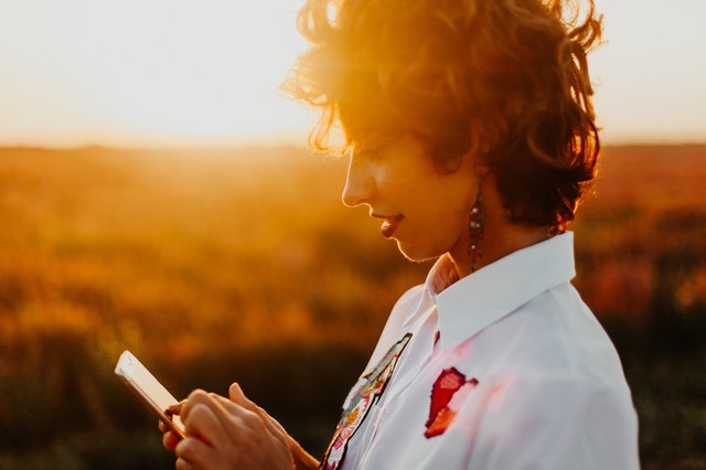 Hip young woman using phone in a sunset field
