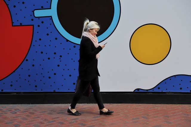 A happy millennial girl walking alongside a mural using her mobile phone