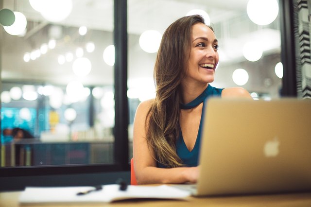 White woman smiling at laptop in modern office setting