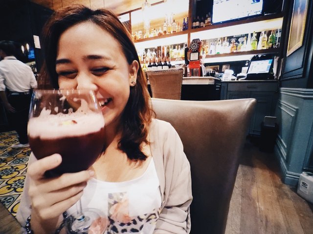 Woman laughing in bar with large glass of red wine