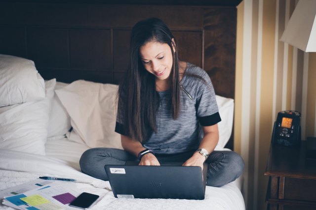 Woman sitting on bed in comfortable clothes doing work at laptop