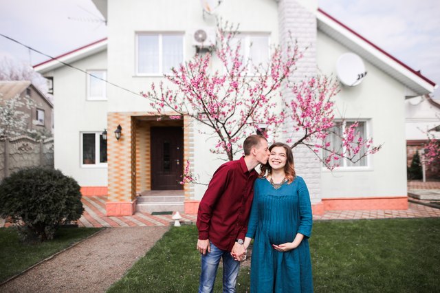 Young white couple standing in front of new house and blossoming tree