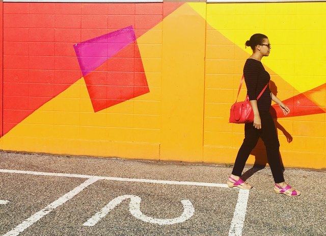 Woman wearing black walking past brightly colored mural