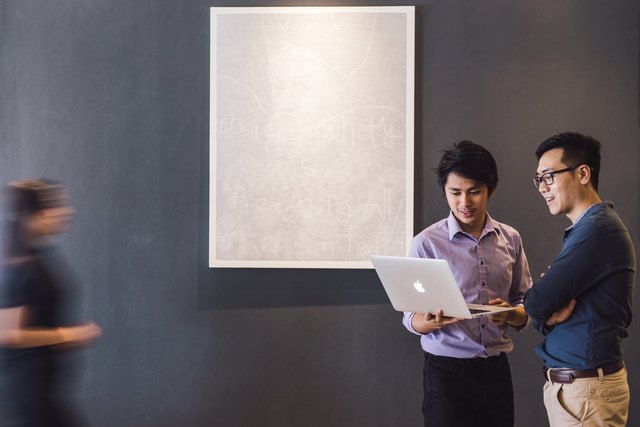 Two employees look at laptop while blurry colleague enters frame