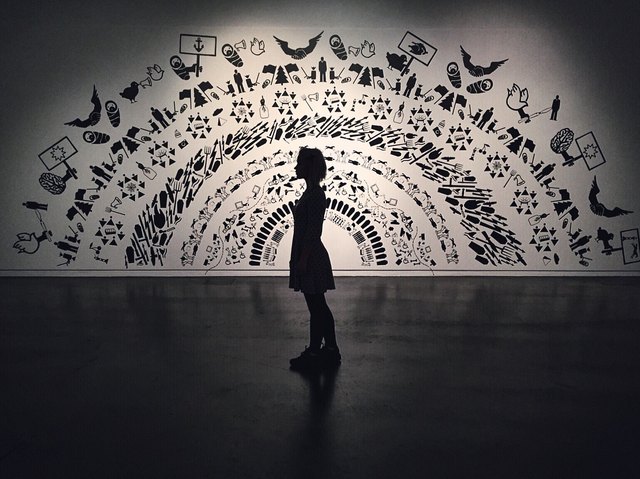 Woman stands in low-lit gallery against monochrome mural