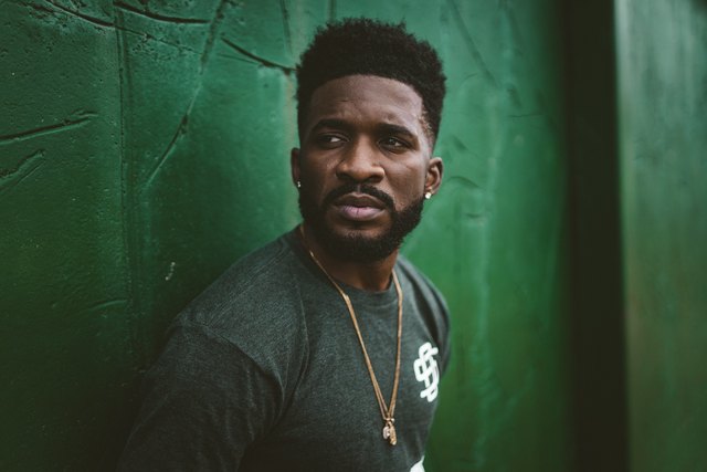 Athletic Black man with beard looking worried in front of green wall