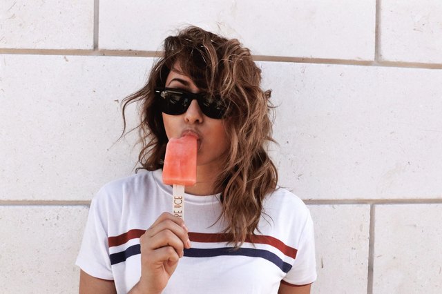 young woman eating popsicle in front of white wall