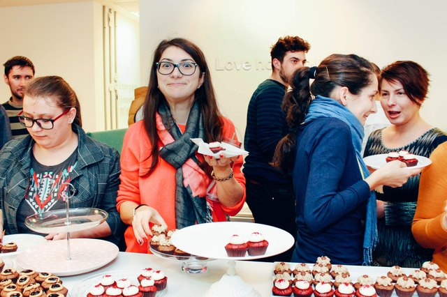 Young woman making a funny face above office party table of cupcakes