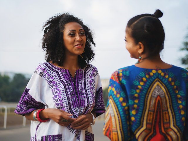 Two Black women wearing colorful shirts conversing