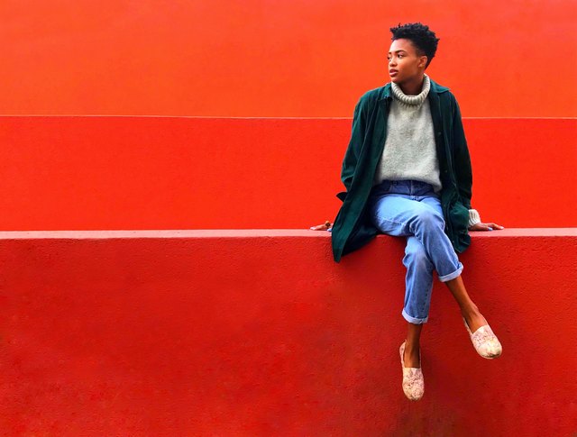 Casually dressed Black woman sitting on red wall against red background