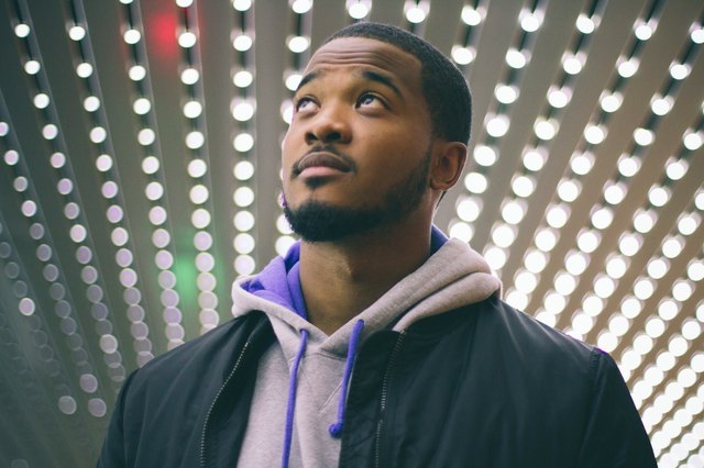 Young Black man looking up against backdrop of rows of lightbulbs