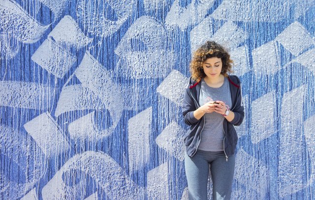 Young woman checking phone in front of blue and white mural