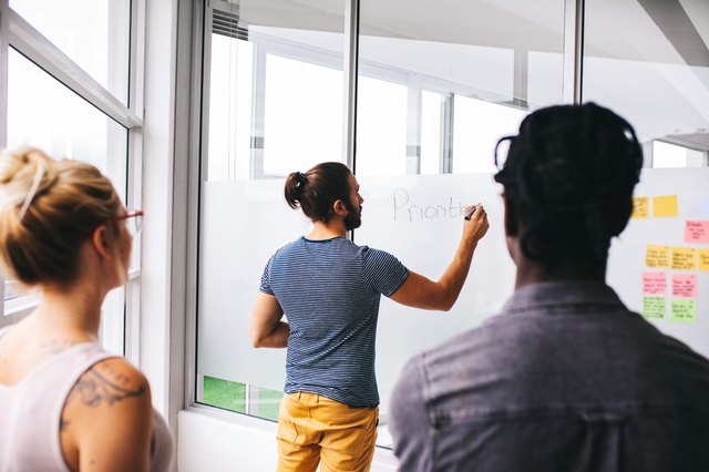 Man writing on whiteboard as a woman and man look on