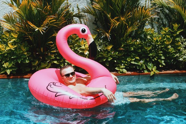 Man relaxing in a tropical pool on a pink flamingo floaty