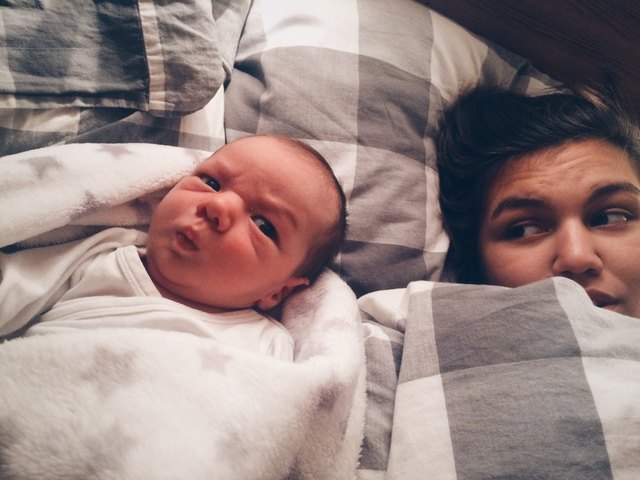 Infant making a funny face on bed next to mother