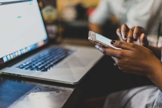 Woman holding phone while sitting in front of laptop
