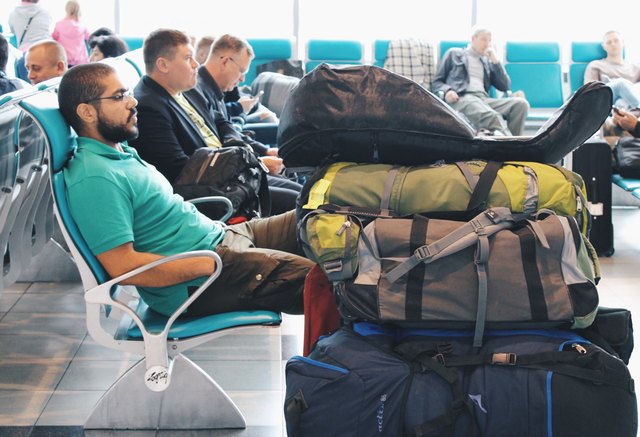 Young bearded man waiting in airport gate near piles of luggage
