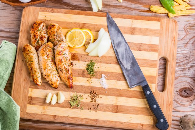 Grilled barbecue chicken breast on a bamboo cutting board on a wooden old table with garlic eggs and vegetables