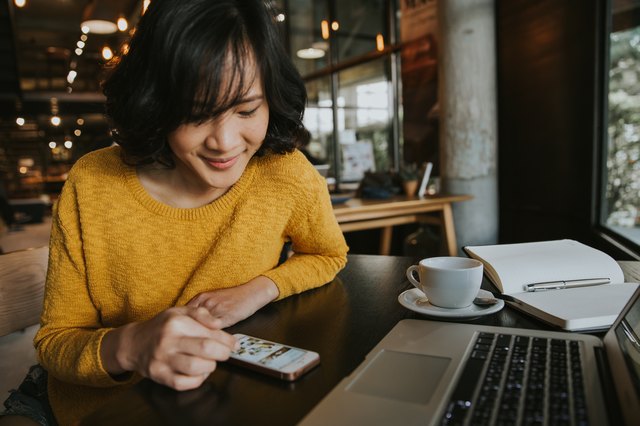 Young woman in coffee shop smiling at phone and laptop
