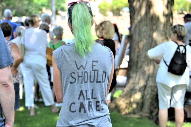 Woman at protest wearing shirt reading "We Should All Care"
