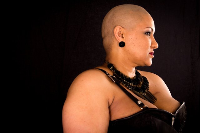 Cancer survivor with shaved head against black background