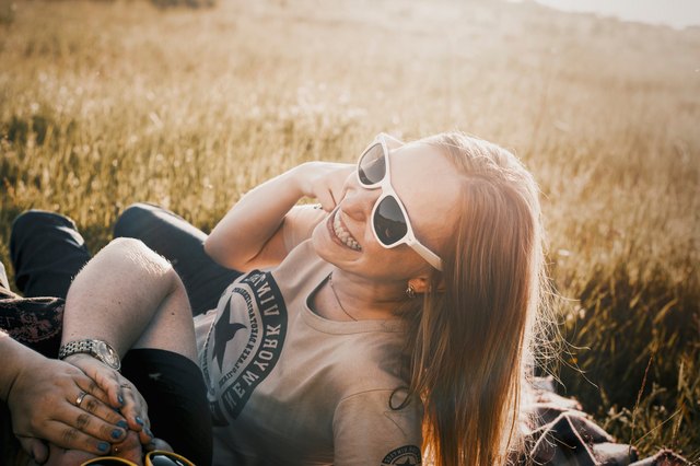Redheaded woman in sunglasses grinning in sunlit field with friend