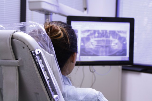 Rear view of woman in dentist's chair looking at mouth x-rays