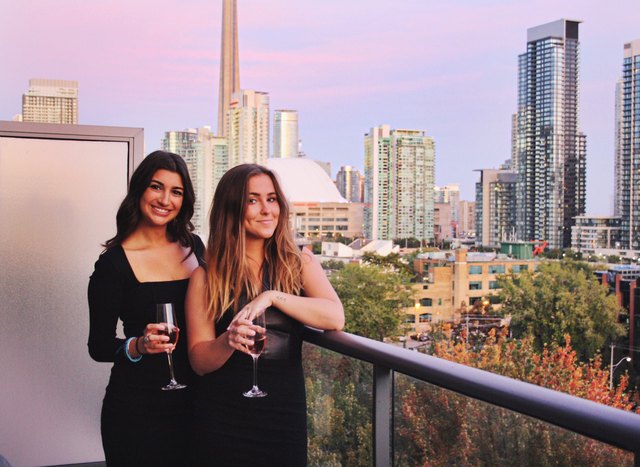 Two young women drinking wine in front of skyline