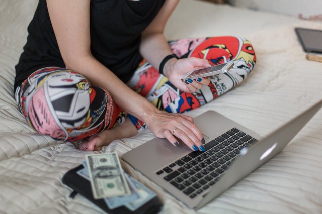 Woman sitting on bed with laptop, phone and cash