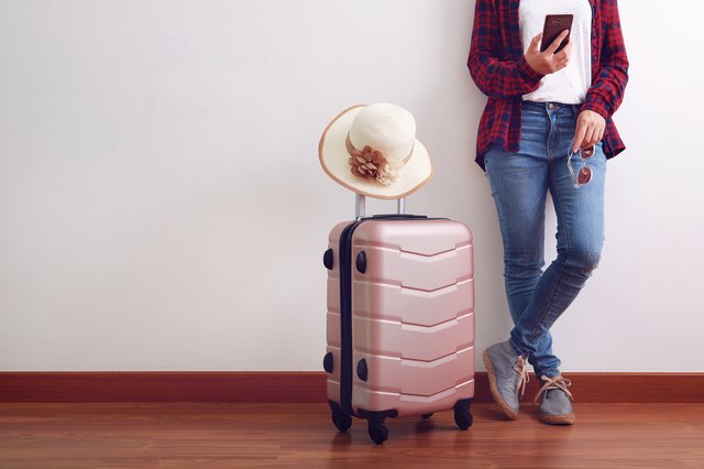 Asian woman traveler looking at smart phone, carry pink luggage with hat