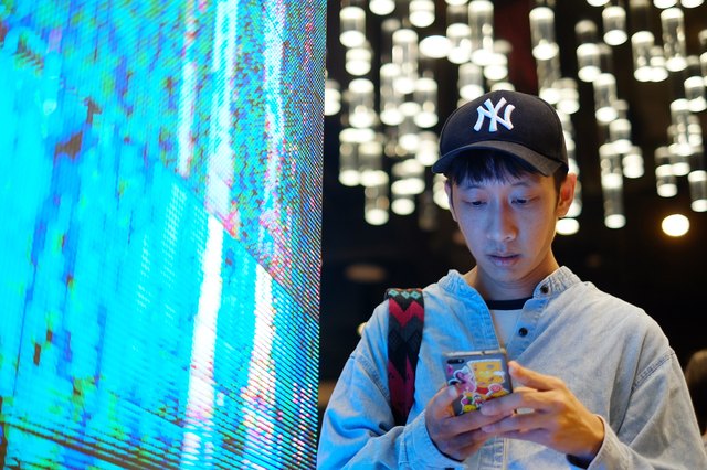 Young man using smartphone next to oversized neon LED light screen