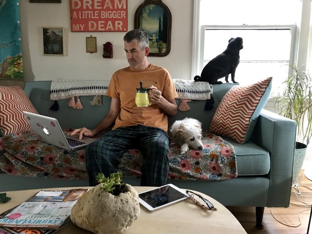 Man in pajamas with dogs, laptop and mug on couch
