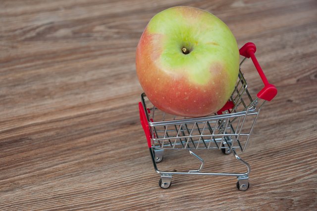 Slik følger du en Vegansk diett når du er brutt AF - budsjett Stor eple legging i handlekurven. Trebakgrunn