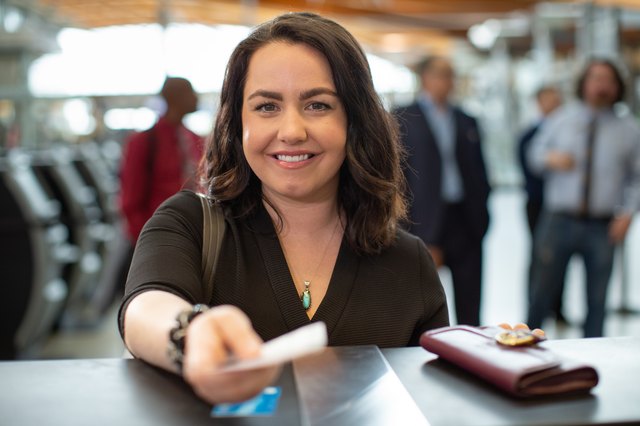 Young woman holding boarding pass smiles at camera at airport check in desk.