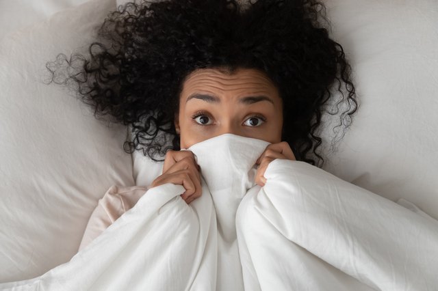 Surprised funny african girl in bed covering face with blanket