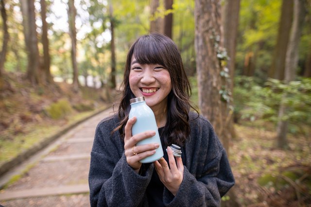 Young woman holding stainless bottle in forest