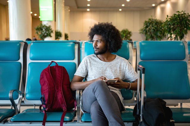 Male traveler at the airport using his cell phone while waiting for his flight