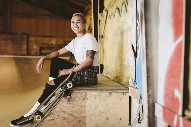 Portrait happy young female skateboarder sitting on ramp at indoor skate park