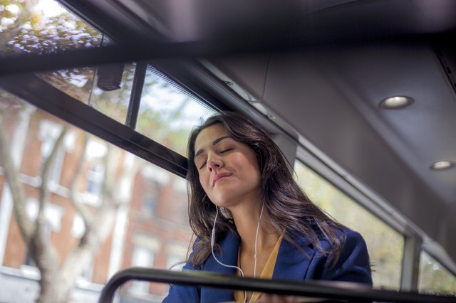 Young woman listening music on a bus with earphones, eyes closed
