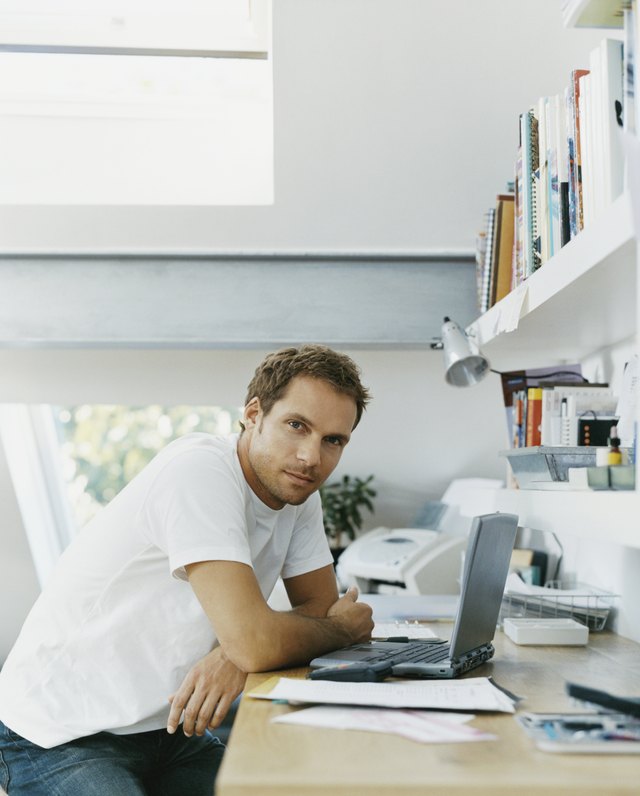 Serious Looking man Sits at his Desk With a Laptop in Front of him