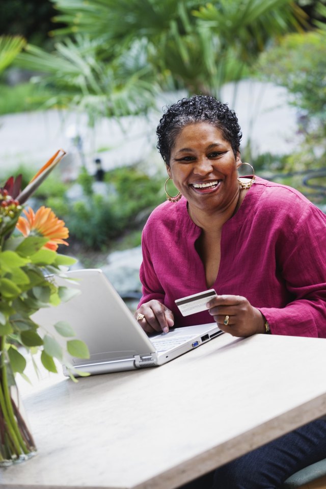 Middle-aged African woman with credit card and laptop outdoors