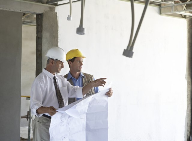 Two Men Standing in a Partially Constructed Room, Holding Blueprints