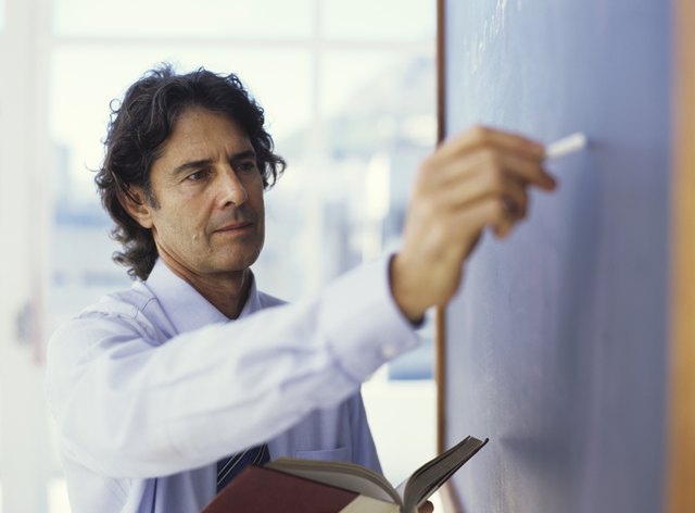 Teacher writing on blackboard and holding book, close up