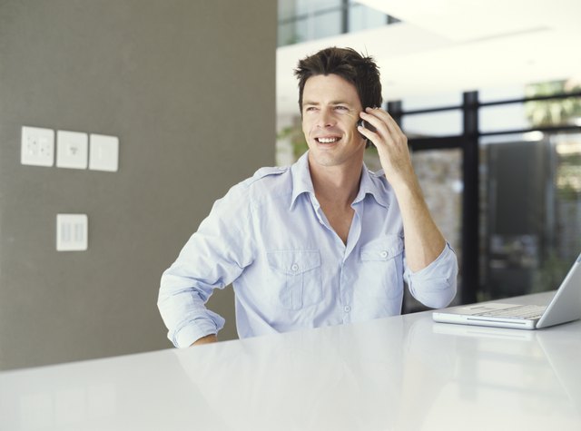 Man with laptop using mobile phone, smiling