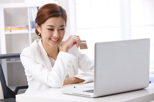 Young business lady holding credit card in front of laptop
