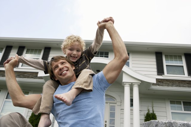 Boy (5-7 years) balancing on father's shoulders outside house, smiling